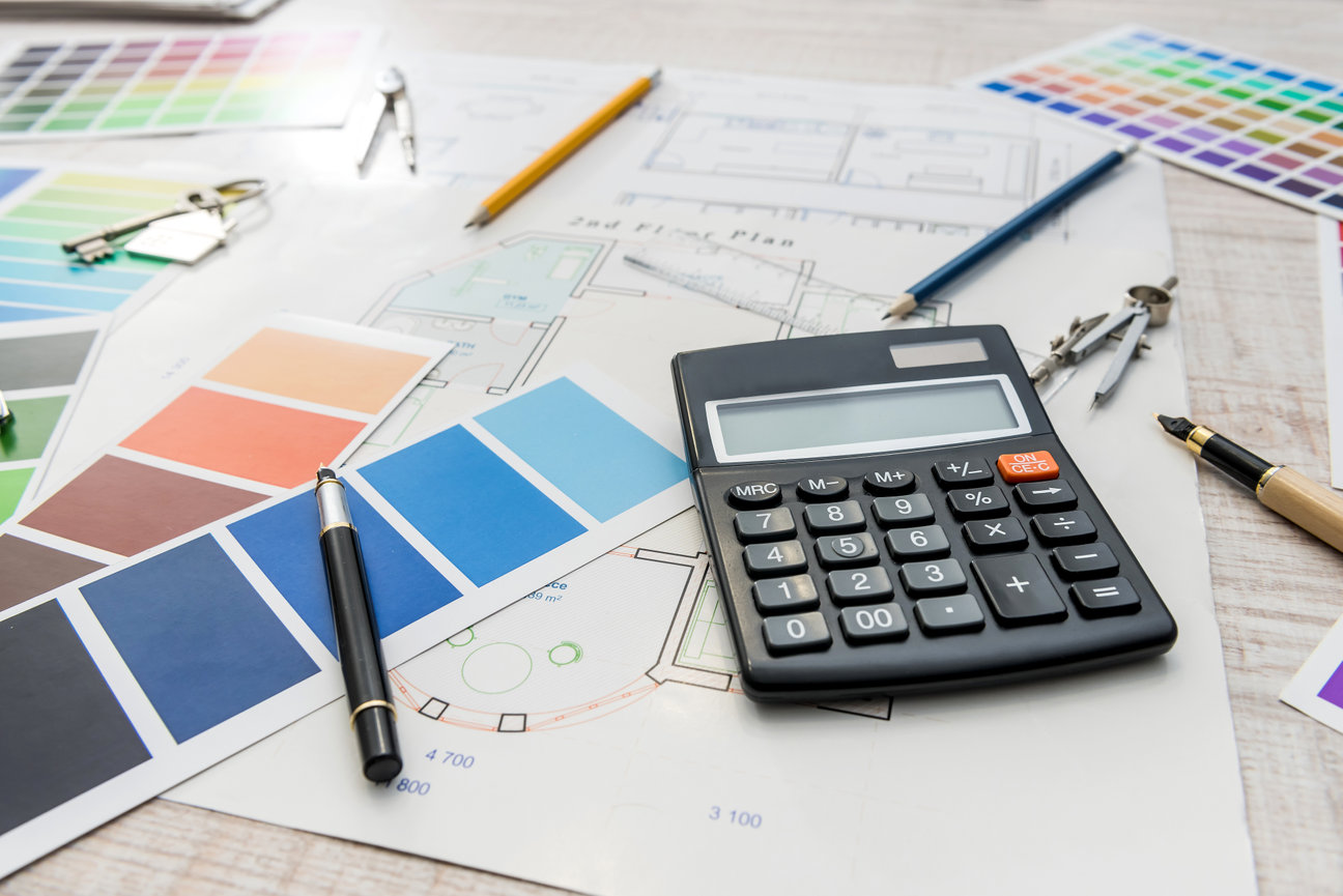 Calculator on architectural plans with paint swatches, pens, and drafting tools.